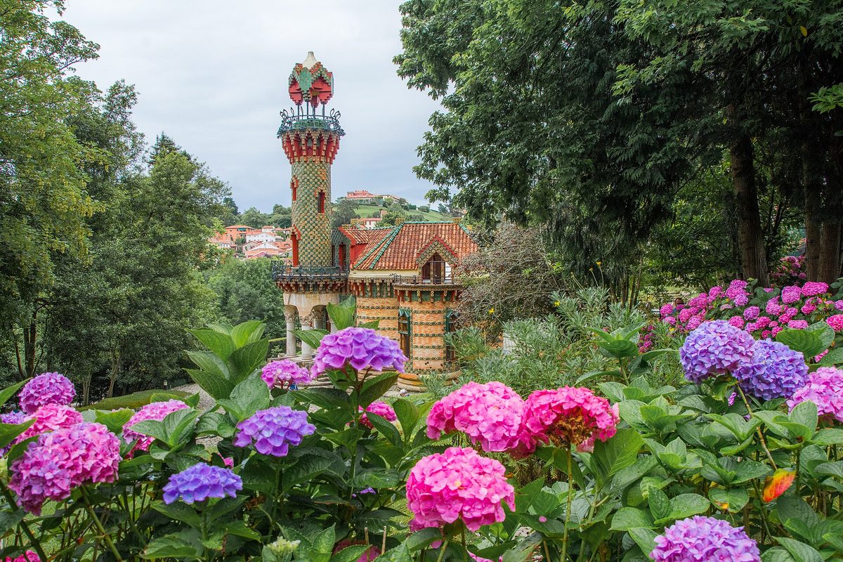 El Capricho de Gaudí, con su torre de cerámica verde, detrás de unas hortensias en flor